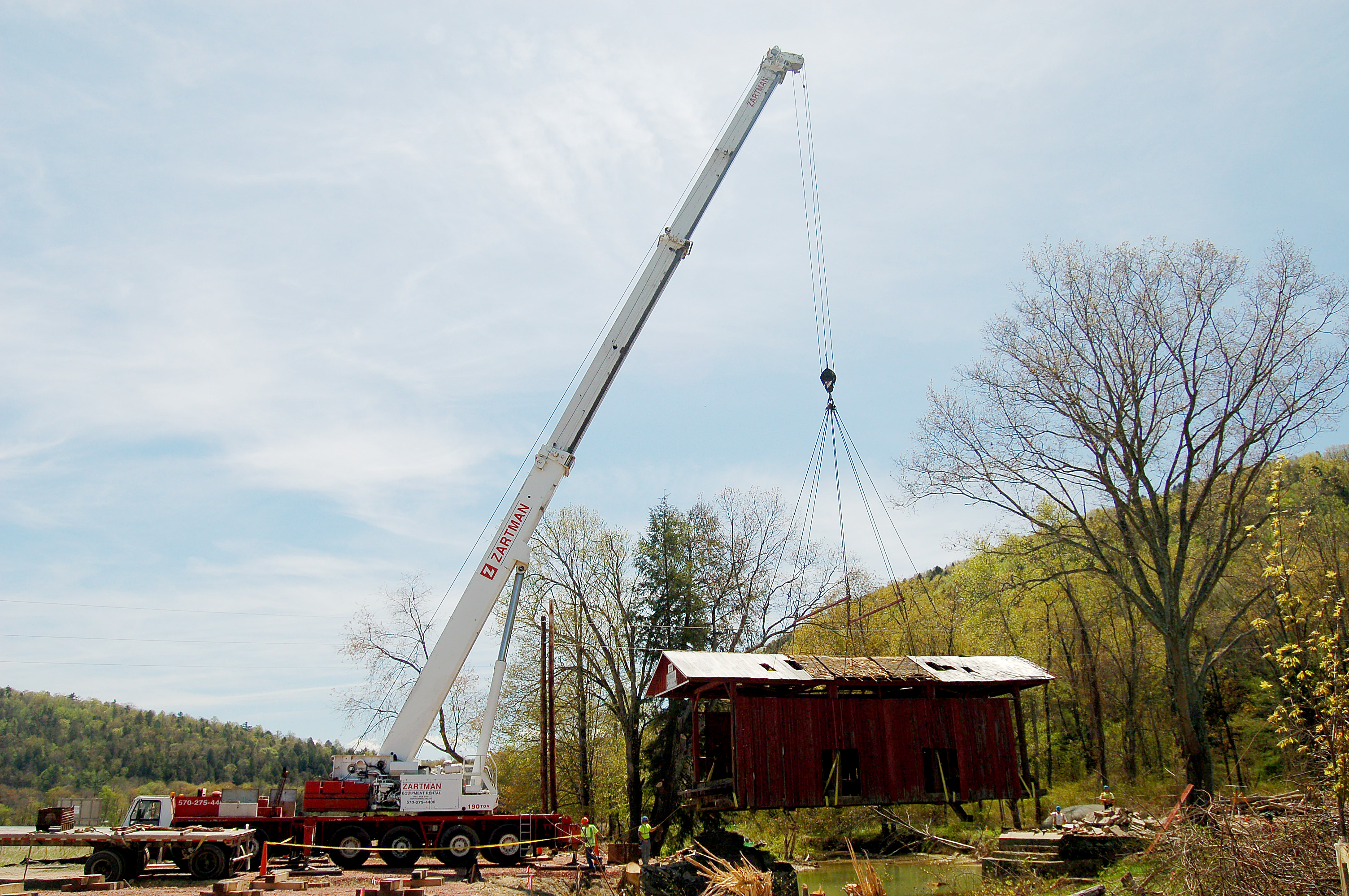 A covered bridge is lifted off its supports and placed on a trailer bed.